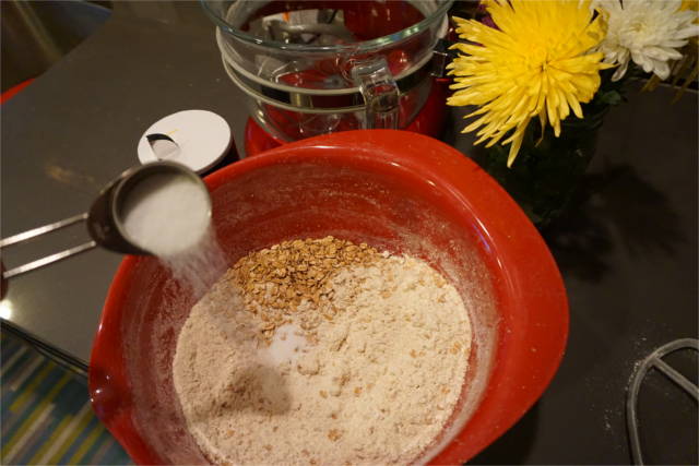 a tablespoon of sugar added to a mixing bowl with spelt flour and spelt flakes