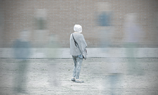 An elderly woman with her back turned and blurry "ghostlike" images of people around her to suggest confusion and dementia